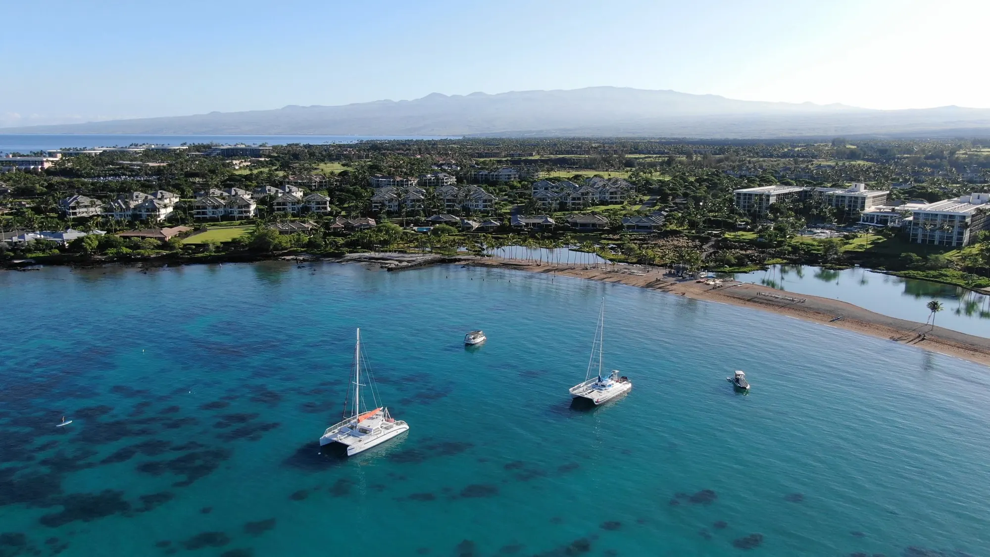 Catamarans anchored in a turquoise bay beside a Hawaiʻi Island resort